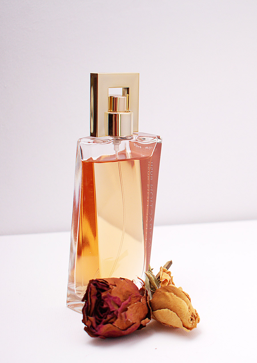 Clear bottle with golden spray pump for perfume in front of two dried roses