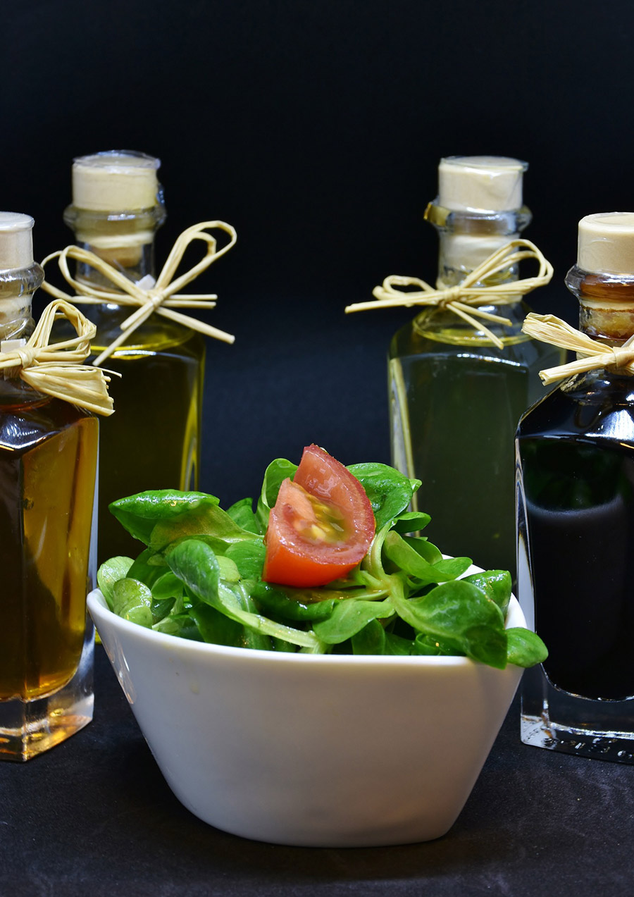 Vier Ölflaschen mit Korkverschlüssen und Schrumpfkapsel um einen Salat